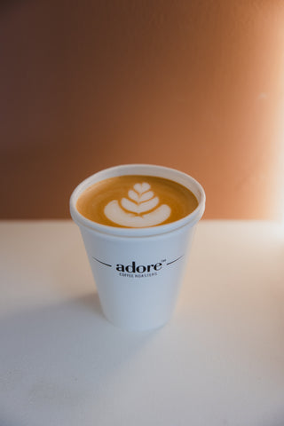 White paper cup with a coffee drink and latte art on a white surface with a blurred background